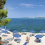 Strand mit Liegen und blauen Sonnenschirmen am klaren Meer bei sonnigem Wetter.