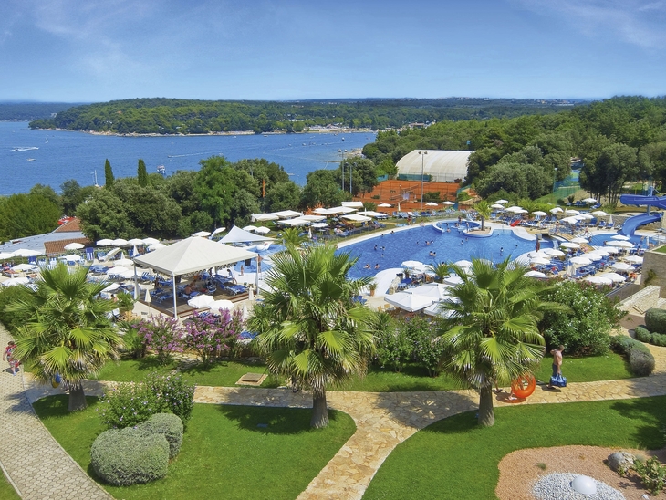 Ferienresort mit Pool, Palmen und Meerblick im Hintergrund.