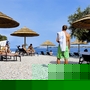 Personen entspannen sich unter Strohdächern am Kiesstrand.