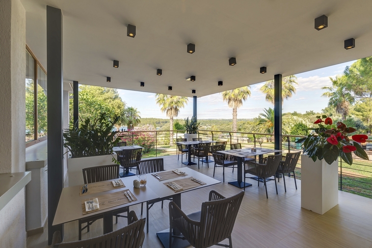 Restaurantterrasse mit Blick auf Palmen und grüne Umgebung.