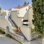 Außenansicht eines mediterranen Gebäudes mit Bäumen und Treppe, zwei Menschen im Freien.