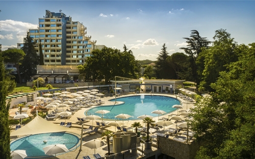 Hotelaußenbereich mit Pool und Sonnenschirmen, grünes Umfeld.