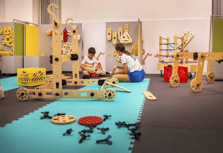 Kinder spielen in einem Raum mit großen Holzbausteinen auf bunten Matten.