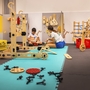 Kinder spielen in einem Raum mit großen Holzbausteinen auf bunten Matten.