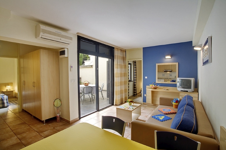 Wohnzimmer eines Ferienapartments mit Sofa, Tisch, Fernseher und Zugang zur Terrasse.