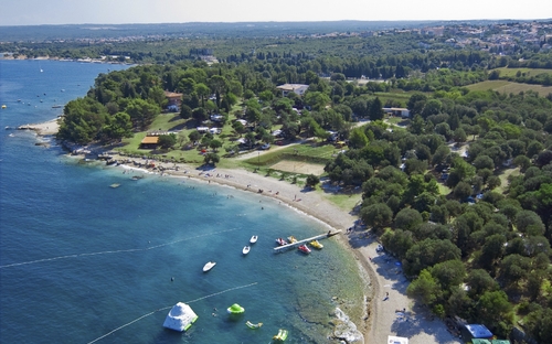 Luftaufnahme von Campingplatz an der Küste mit Bäumen und Freizeitmöglichkeiten am Strand.