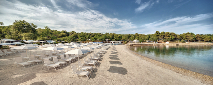 Sandstrand mit weißen Liegestühlen und Sonnenschirmen am Lanterna Premium Camping Resort.