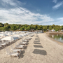 Sandstrand mit weißen Liegestühlen und Sonnenschirmen am Lanterna Premium Camping Resort.