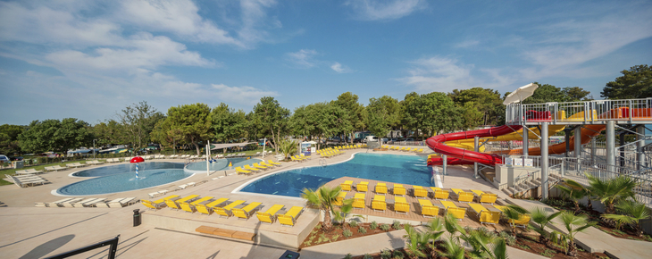 Poolanlage mit Liegestühlen und Wasserrutschen in einem Camping-Resort.