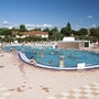 Menschen schwimmen und entspannen in einem Außenpool bei sonnigem Wetter.