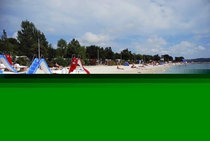 Strand mit Tretbooten und Badegästen am Meer an einem sonnigen Tag.