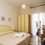 Helles Hotelzimmer mit Bett, Schrank, Tisch, Spiegel und Blumen.