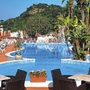 Hotelpool mit Liegestühlen und Sonnenschirmen, umgeben von Pflanzen und Bäumen.