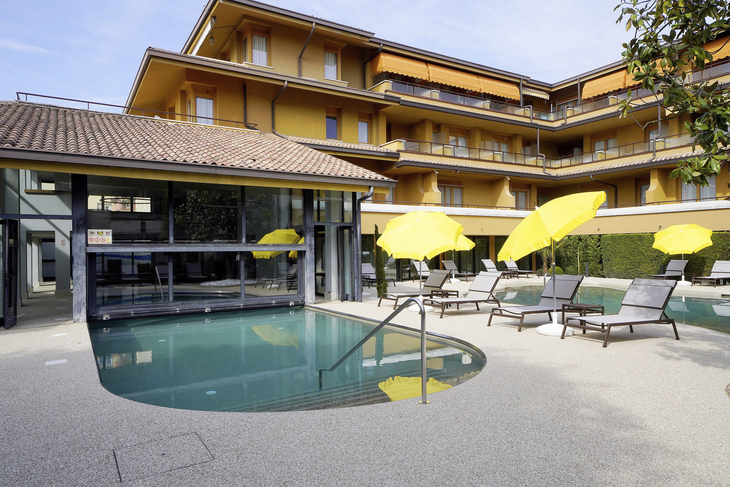 Außenbereich eines Hotels mit Pool, gelben Sonnenschirmen und mehrstöckigem Gebäude.