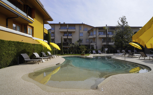 Hotelpool mit gelben Sonnenschirmen und Liegestühlen, umgeben von Gebäuden.