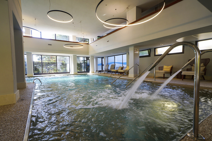 Innenpool mit Wasserstrahlen und Liegestühlen im Hotel.