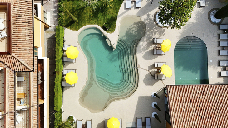 Luftaufnahme von zwei Pools und gelben Sonnenschirmen in einem Hotel in Bardolino.