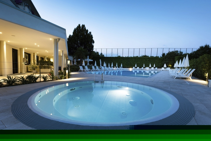 Runder Pool bei Abenddämmerung vor Hotel mit Liegestühlen und Pflanzen.
