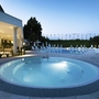 Runder Pool bei Abenddämmerung vor Hotel mit Liegestühlen und Pflanzen.