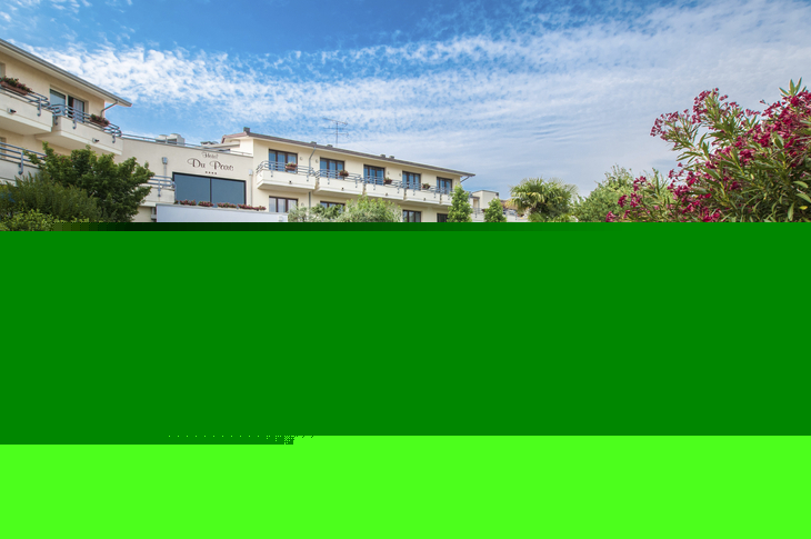 Fassade eines Hotels mit gepflegtem Garten und blühenden Pflanzen.