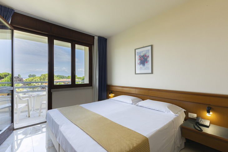 Hotelzimmer mit Doppelbett, Fenster mit Blick auf Balkon und Landschaft.