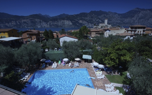 Blick von oben auf einen Pool mit Liegestühlen, umgeben von Bäumen und Häusern in Malcesine.