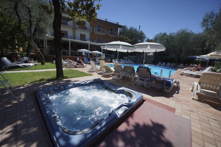 Hotelpool mit Liegestühlen und Whirlpool in Malcesine bei sonnigem Wetter.