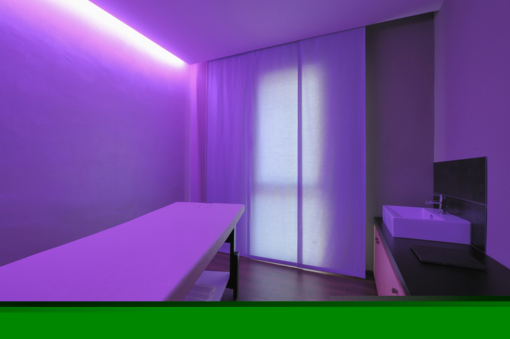 Beleuchteter Massageraum mit lila Licht und Waschbecken.