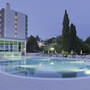 Nachtansicht eines beleuchteten Hotelpools mit Liegestühlen und Bäumen im Hintergrund.