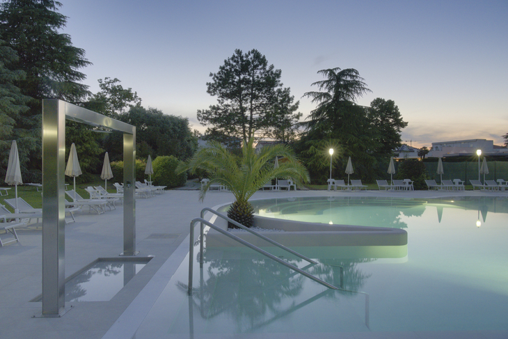 Beleuchteter Pool bei Nacht in einem Hotel mit umgebenden Pflanzen und Palmen.