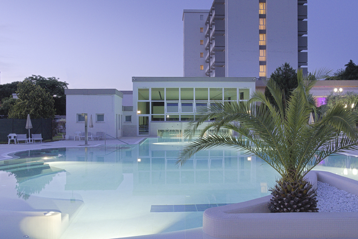 Außenansicht des Hotelpools bei Tag mit Palmen und modernem Gebäude im Hintergrund.