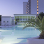 Außenansicht des Hotelpools bei Tag mit Palmen und modernem Gebäude im Hintergrund.