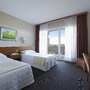 Hotelzimmer mit zwei Einzelbetten, Schreibtisch und Balkon mit Vorhängen.
