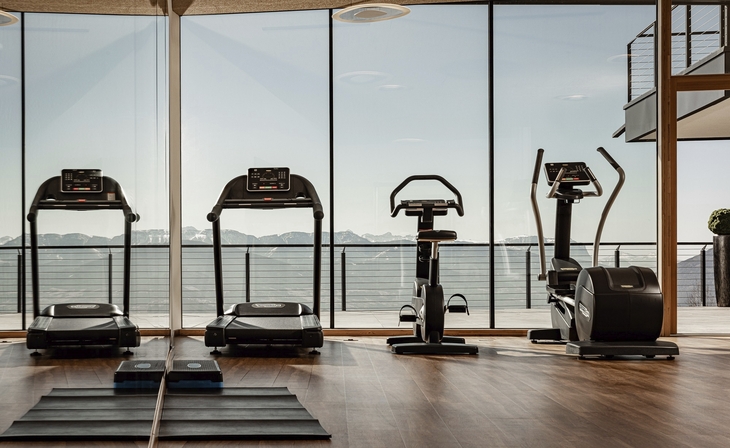 Innenraum eines Fitnessstudios mit Trainingsgeräten vor Panoramafenster.