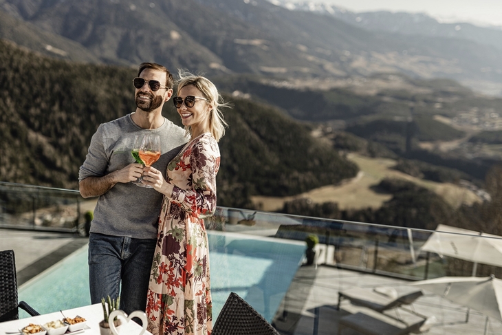 Paar genießt Aperol vor Infinitypool mit Panoramablick auf Berge.