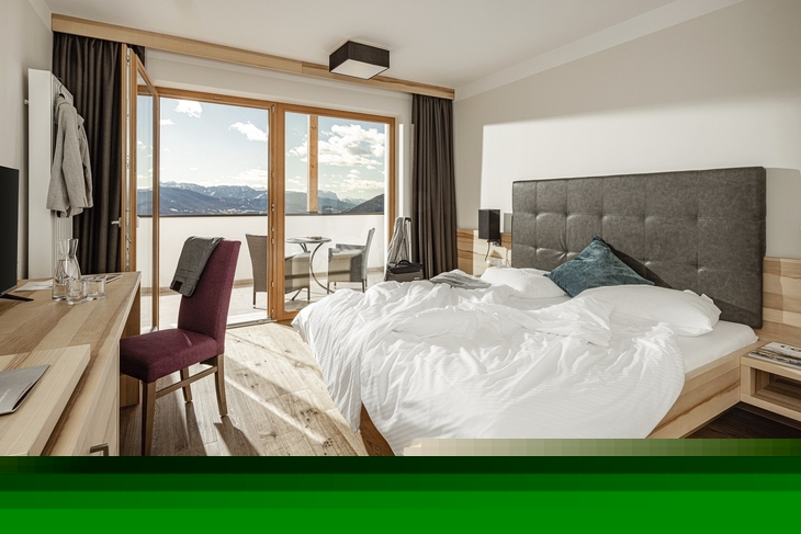 Doppelzimmer mit Bett und Balkonausblick auf Berge.