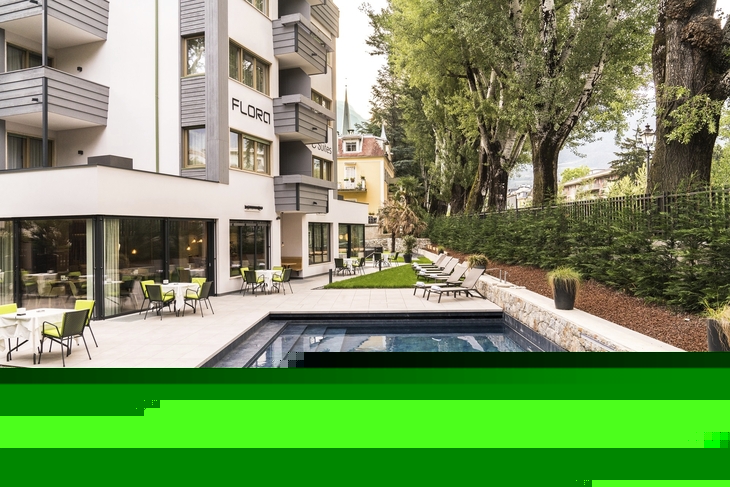 Außenbereich des Hotels Flora mit Pool und Liegen im Garten.