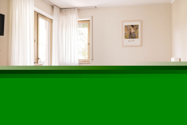 Doppelzimmer mit Bett, Tisch und Stuhl, helle Vorhänge und Bild an der Wand.