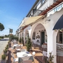 Hotelterrasse mit Tischen und Stühlen unter Arkaden, sonniger Tag.