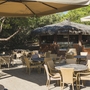 Terrasse mit Tischen und Stühlen, Strohdach-Gebäude im Hintergrund.