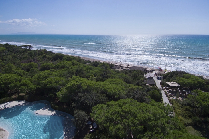 Blick auf bewaldeten Küstenbereich mit Strand und Meer im Hintergrund.