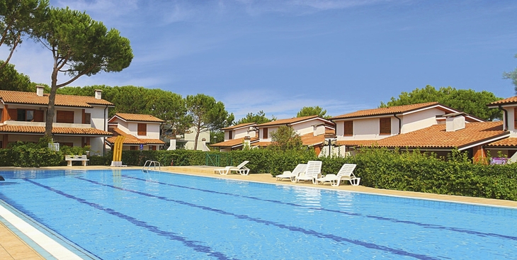 Ein Ferienhauskomplex mit einem großen Pool und Liegestühlen unter blauem Himmel.