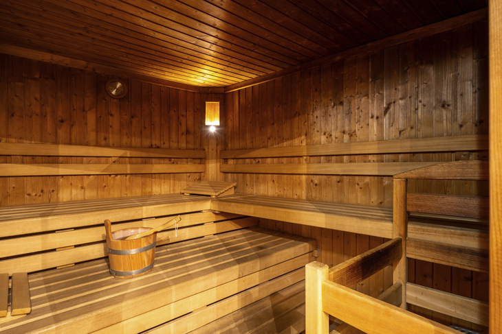 Innenansicht einer Holzsauna mit Bänken und einem Eimer auf der Bank.