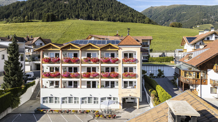 Fassade eines Hotels mit Balkonen und Blumenkästen vor einer grünen Hügellandschaft.