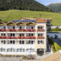Fassade eines Hotels mit Balkonen und Blumenkästen vor einer grünen Hügellandschaft.
