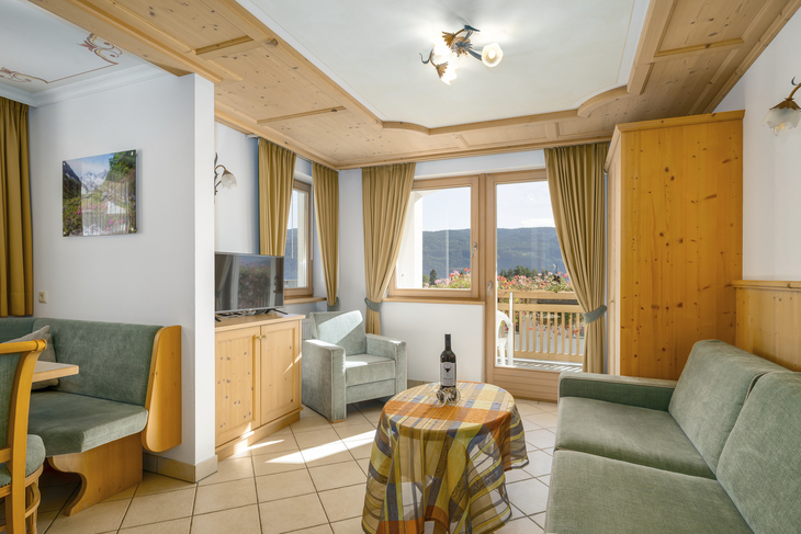 Helles Wohnzimmer mit Sofas, Tisch, Fernseher und Balkonblick auf Berge.