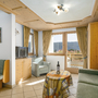 Helles Wohnzimmer mit Sofas, Tisch, Fernseher und Balkonblick auf Berge.
