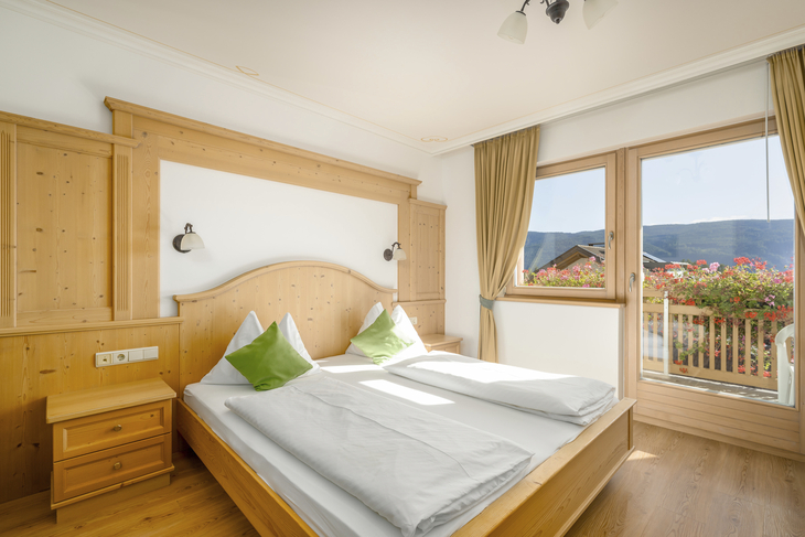 Helles Schlafzimmer mit Holzmöbeln, Doppelbett und Aussicht auf Berge durch Fenster.