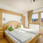 Helles Schlafzimmer mit Holzmöbeln, Doppelbett und Aussicht auf Berge durch Fenster.