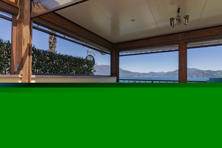 Terrasse eines Restaurants mit Seeblick, gedeckte Tische, Berge im Hintergrund.